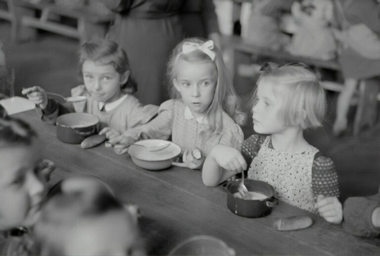 Three young girls at a table eating and are at risk for eating disorders.