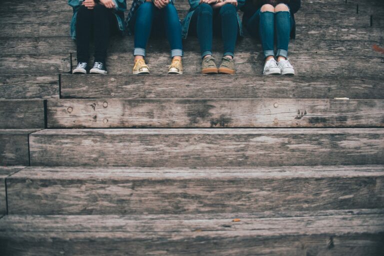 A photo of four girls of the tween years are sitting on a step, with just their legs showing from the knee down. They represent some of the influences on body image at that age.