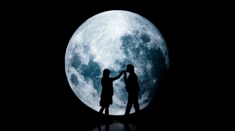 Sillhouette of a couple dancing together in the front of a large moon.