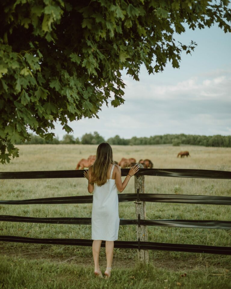 A woman who appears to be a Highly Sensitive Person leaning against a fence watching horses