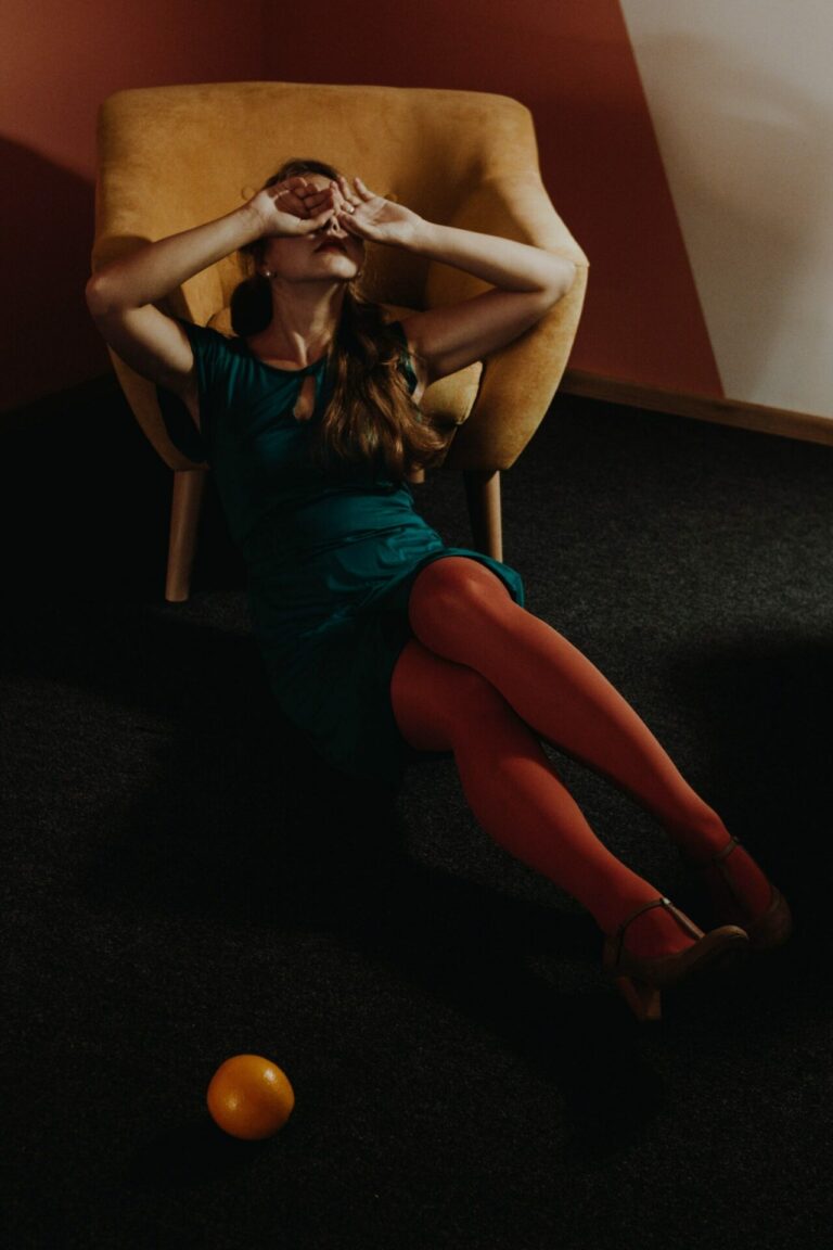 A photo of an exhausted stressed out woman, outstretched partially in a chair and on the ground, who could be experiencing burn out